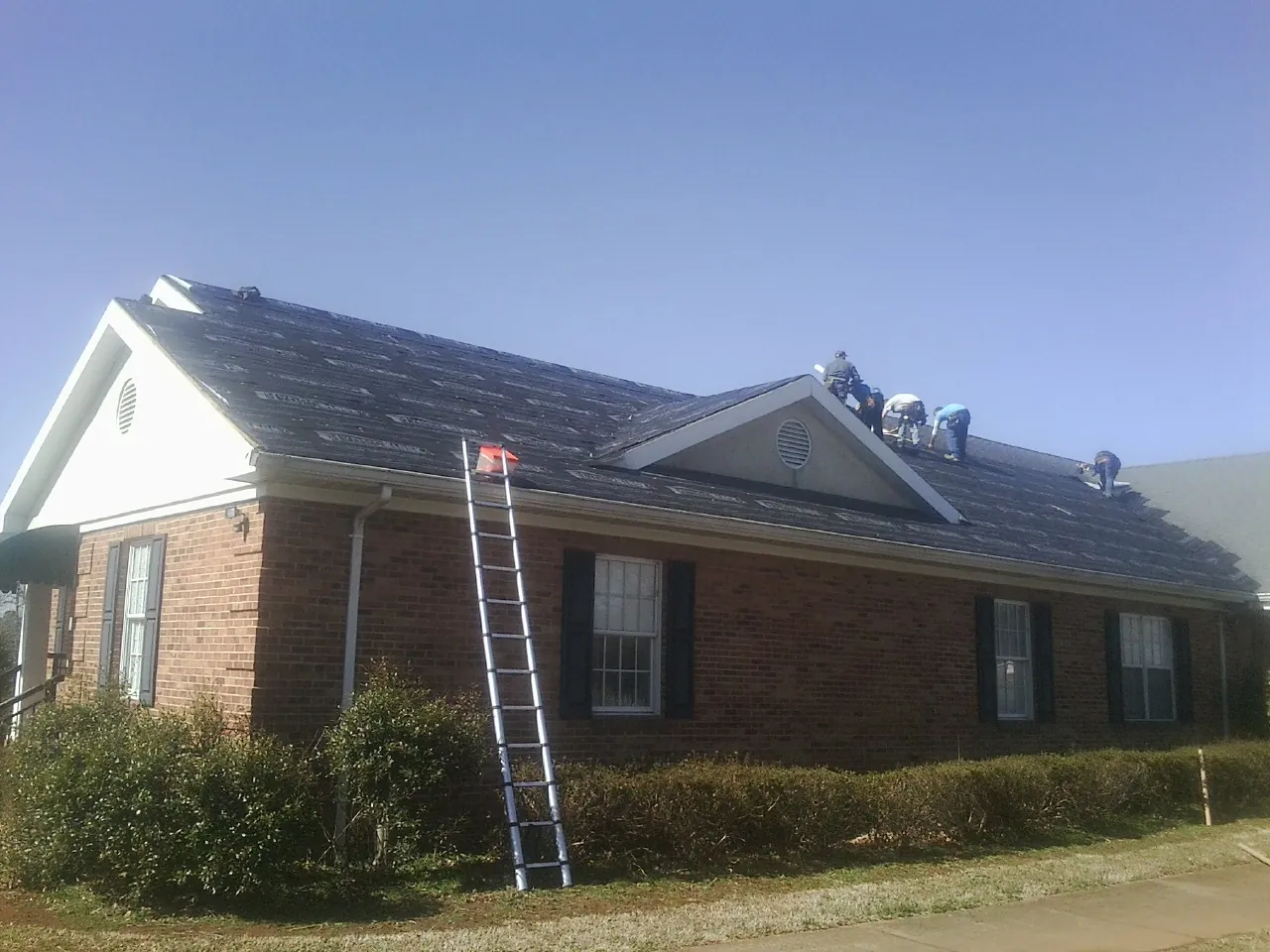 Crew tearing shingles off a brick ranch roof with a ladder set — Emergency Roof Repair work by our crew in Binghamton