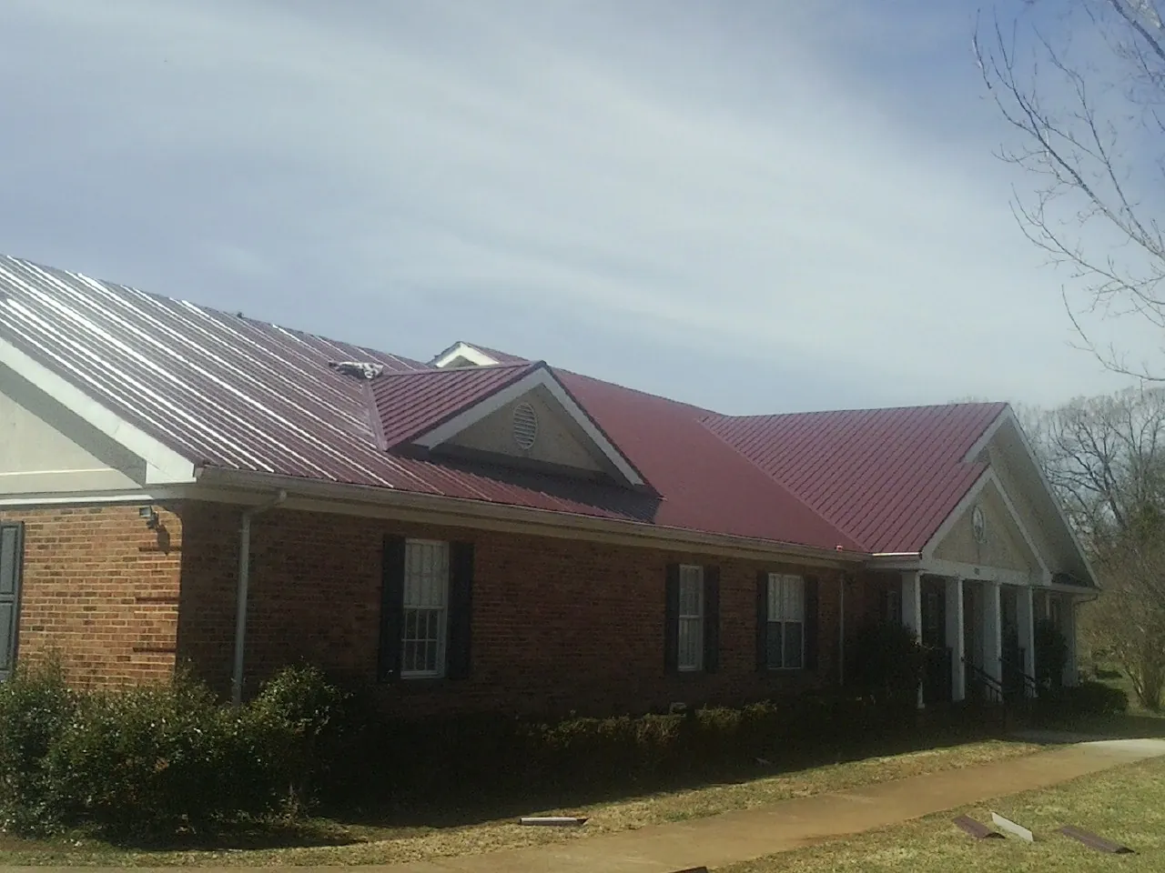 Red metal roof with gabled entries on a long brick building, from a Hail Damage Roof Repair job in Binghamton