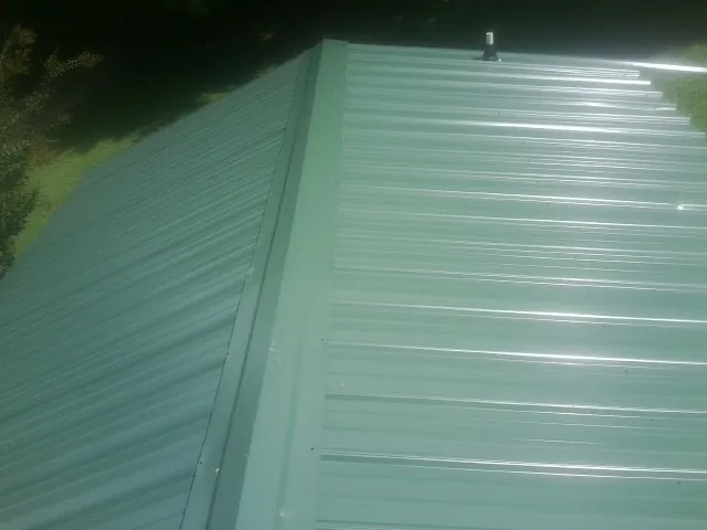 New green metal panels meeting at the ridge of a roof — Flat Roof Repair work by our crew in Binghamton