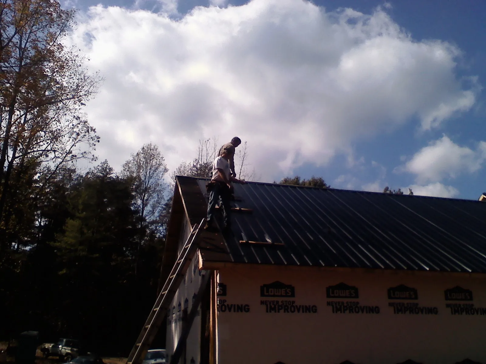 Roofer fastening dark metal panels high against a cloudy sky, from a Roof Inspection job in Binghamton
