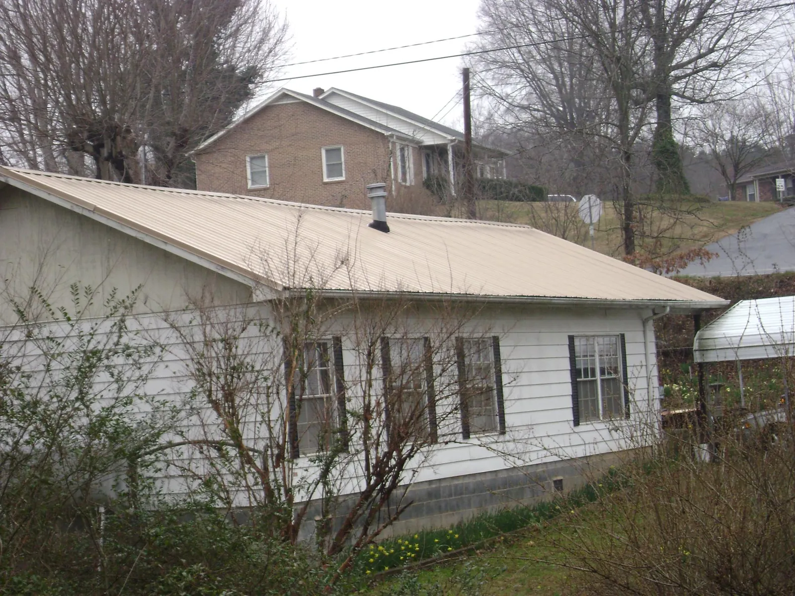 Tan metal roof on a white sided house set into a hillside — Commercial Roofing by Roofing Brothers in Binghamton