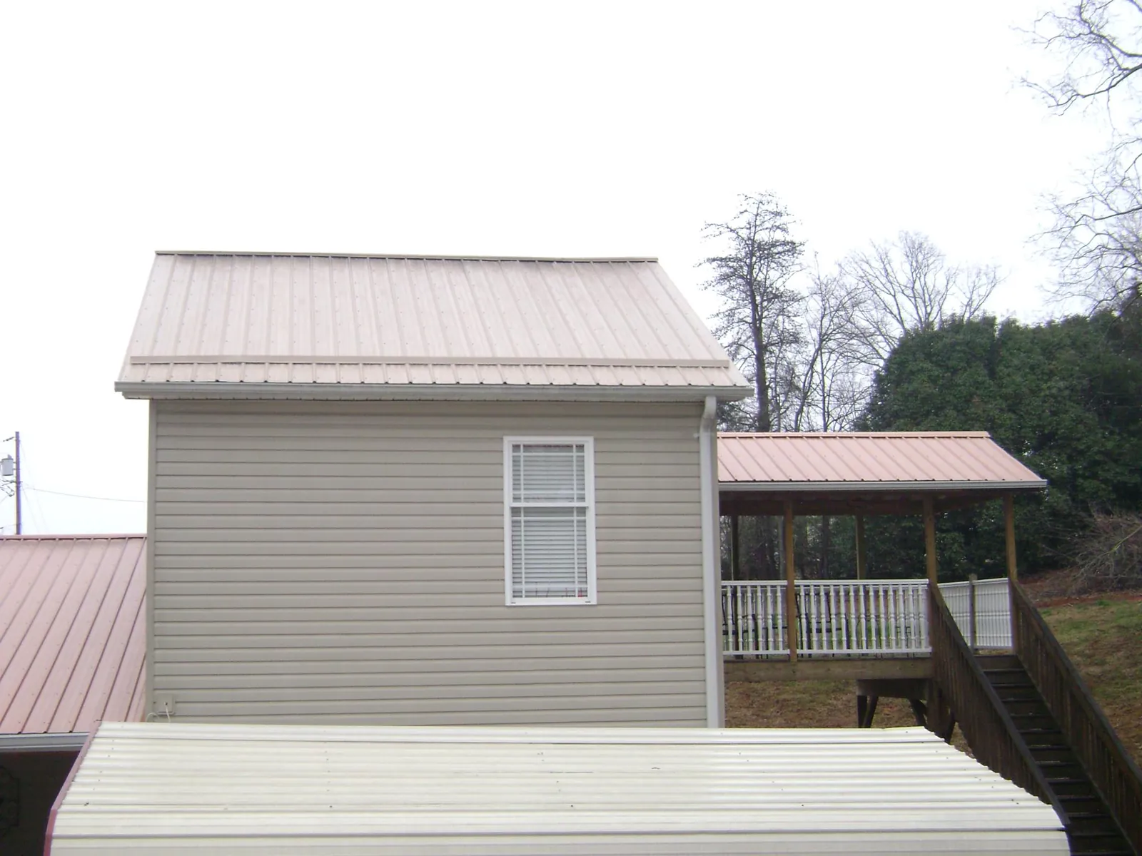 Tan metal roofs on a two story addition and attached porch, from a Roof Replacement job in Binghamton