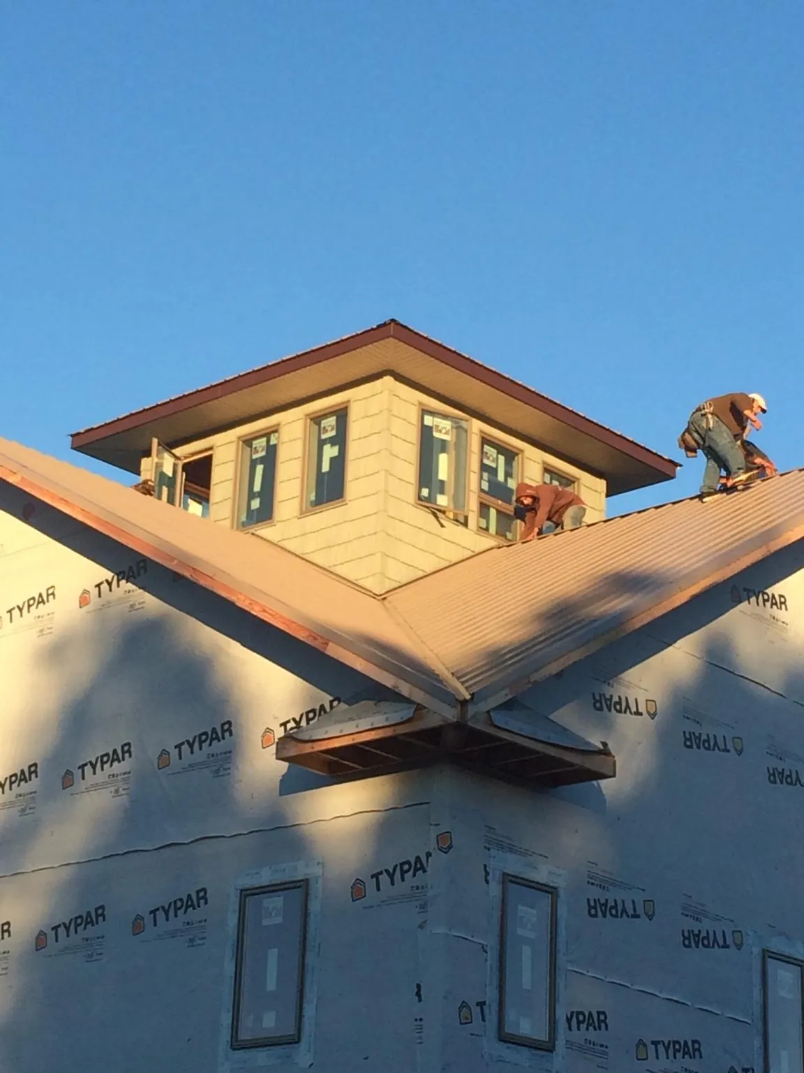 Roofers working around a rooftop cupola on a new metal roof at sunset — Roof Waterproofing in Binghamton by Roofing Brothers